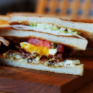 Close-up of a sandwich with egg, bacon, and fresh vegetables on a wooden board.