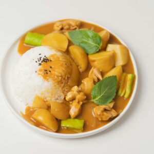 From above of appetizing dish of Indian cuisine curry made of vegetables and meat and served with rice and green leaves
