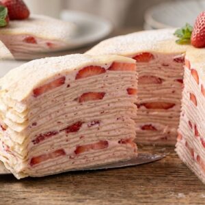 mille crepe cake, strawberry cake, layered cake, cake slice, fresh strawberries, dessert, pastry cream, sweet treat, mint leaves, elegant dessert, powdered sugar, cake server, wooden table, afternoon tea, baking art, cake presentation, delicate pastry, cake cross section, cake serving, kitchen