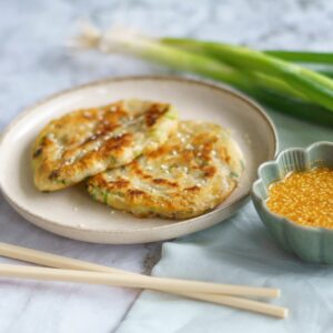 Tasty Korean scallion pancakes served with sesame dipping sauce on a ceramic plate, styled with chopsticks.