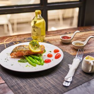 High angle of served plate with fried fish and vegetables placed near saucers with spices and olive oil